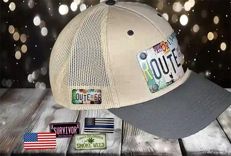 Beige mesh baseball cap with Route 66 novelty hat pins and custom license plate pins on a wood surface.