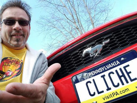 Man smiling next to red Ford Mustang with Pennsylvania novelty license plate reading CLICHE