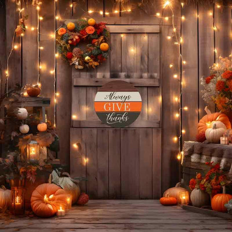 Rustic fall porch with pumpkins, autumn wreath, string lights, and an 'Always Give Thanks' sign.