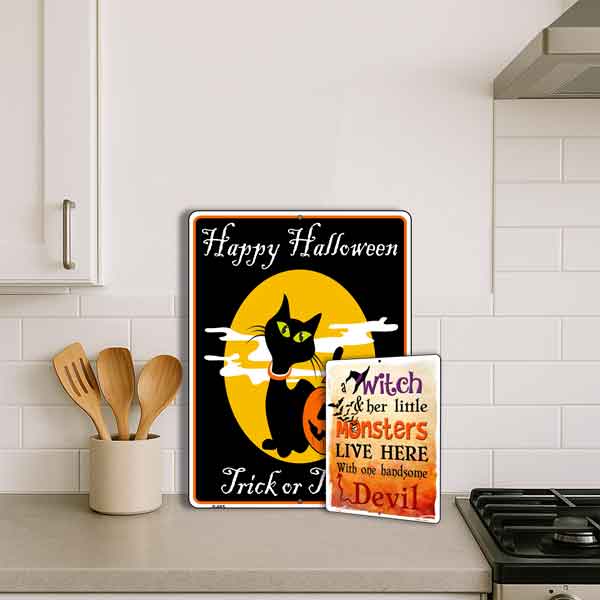 Two Halloween-themed signs on a kitchen counter with utensils and a stove.